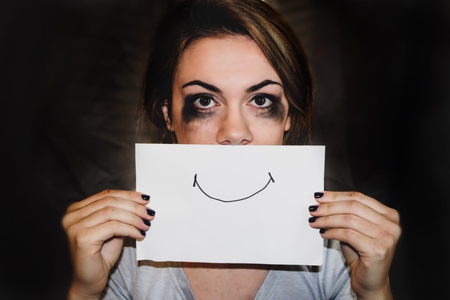 Youthful woman holding a piece of paper with a smile drawn in front of her face.